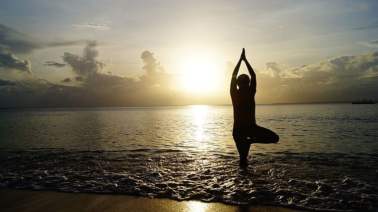 Der Baum am Strand – Yogaübung für Einsteiger am Rand des Ozeans bei Sonnenaufgang.