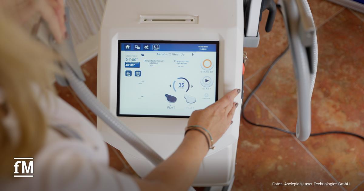 Eine Person bedient ein Bodyforming-Gerät von BodyLab mit Touchscreen. Auf dem Bildschirm sind Einstellungen wie 'Amplitude', 'Frequenz' und 'Heat Up' zu sehen.