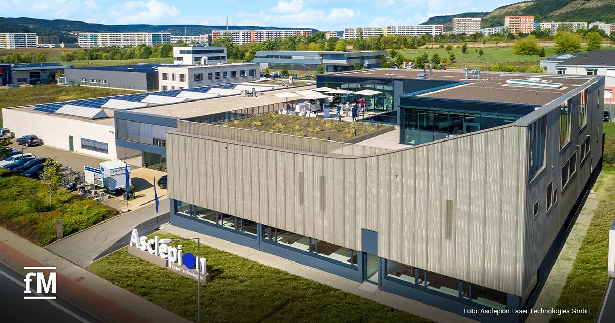 Luftaufnahme des modernen Asclepion-Firmensitzes mit großer Fensterfront und begrüntem Dach. Menschen versammeln sich auf der Dachterrasse. Im Bild sind die Logos „BodyLab“ und „fM“ eingeblendet