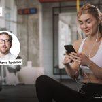 Junge Frau im Sportoutfit nutzt ein Smartphone im Fitnessstudio, eingeblendet ist ein Porträt von Prof. Dr. Marco Speicher mit Namensschriftzug.