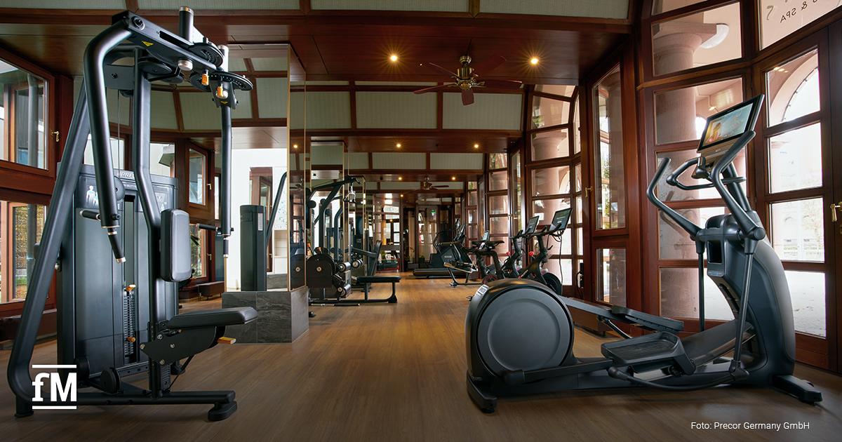 Ein stilvoll eingerichteter Fitnessraum mit Holzboden und Panoramafenstern, ausgestattet mit Kraft- und Ausdauergeräten.