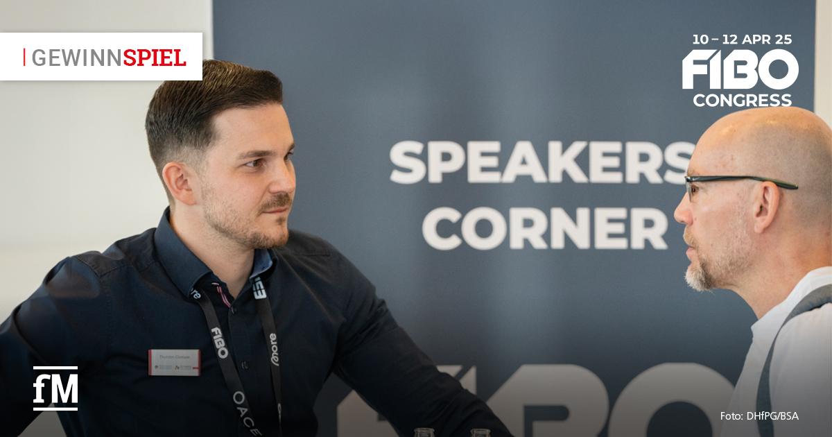 Zwei Männer im Gespräch beim FIBO Congress 2024, im Hintergrund das Schild „Speakers Corner“. Links trägt ein Mann ein Namensschild und dunkles Hemd. Rechts ein Mann mit Brille und Glatze. Links oben steht ein Gewinnspielhinweis. Rechts oben des FOBO Congress-Logo für 2025