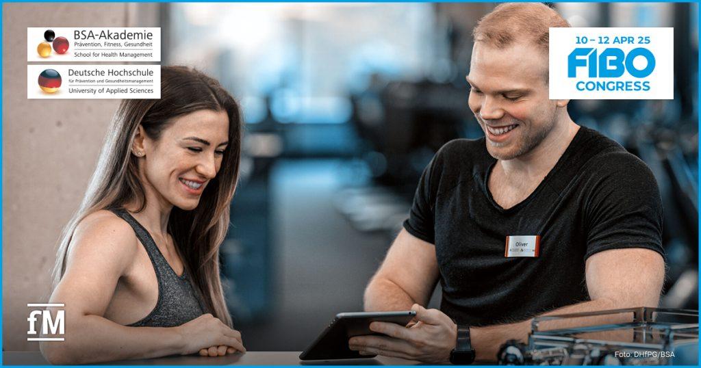 Ein lächelnder Trainer zeigt einer sportlich gekleideten Frau ein Tablet. Beide stehen in einem modernen Fitnessstudio. Logos der BSA-Akademie, DHfPG und des FIBO Congress 2025 sind zu sehen.