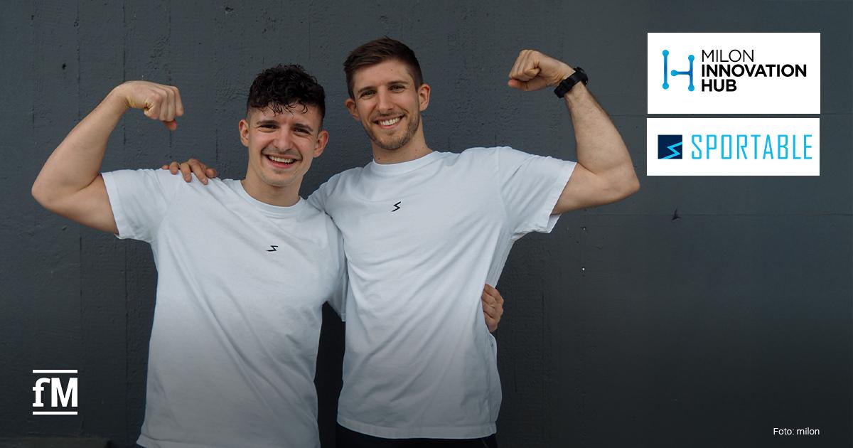 Zwei junge Männer in weißen T-Shirts stehen lachend vor einer grauen Wand und zeigen muskulös ihre Arme. Rechts oben sind die Logos von „milon Innovation Hub“ und „SPORTABLE“ sichtbar.