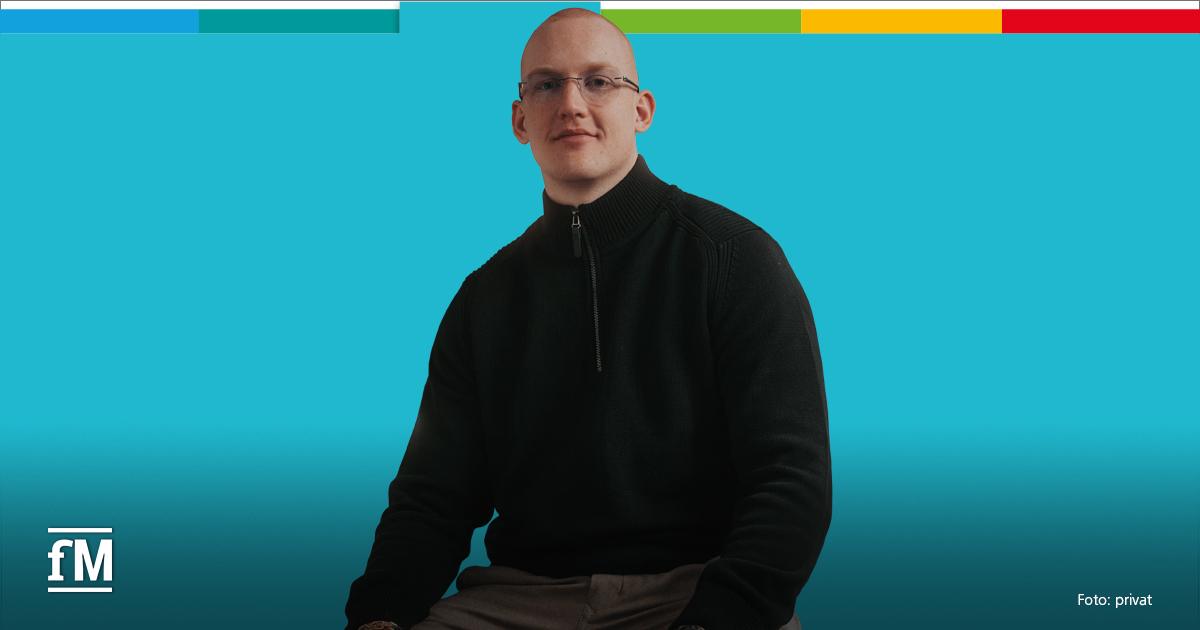 Ein junger Mann mit Brille sitzt vor einem einfarbig türkisen Hintergrund. Er trägt einen dunklen, hochgeschlossenen Pullover mit Reißverschluss und schaut ruhig in die Kamera.