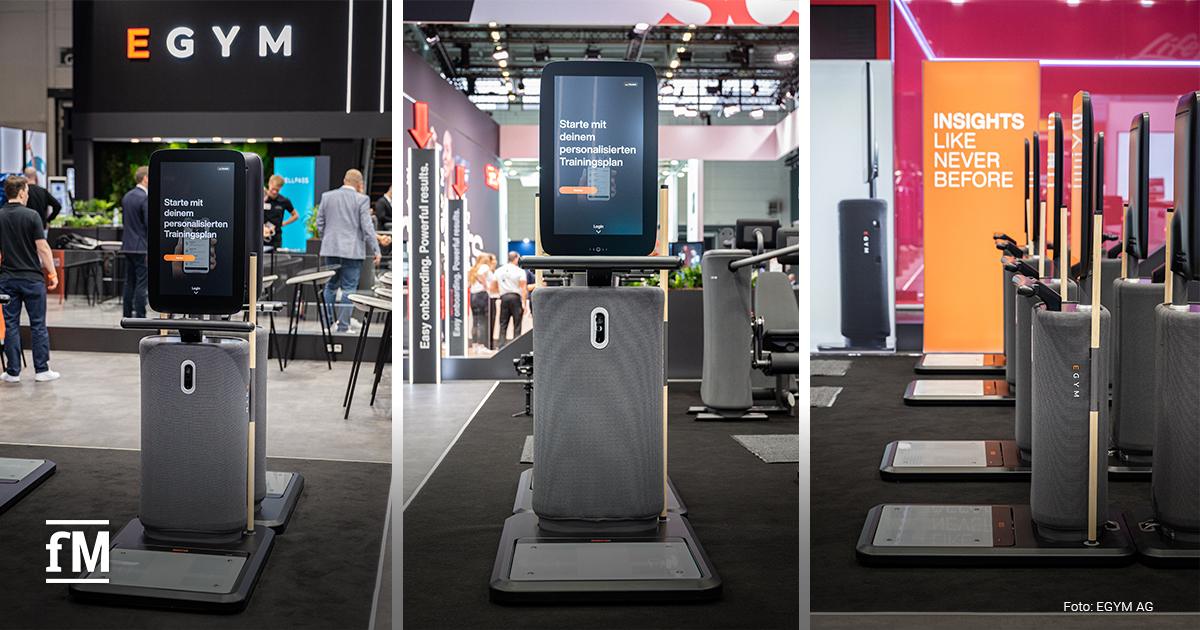 Drei Ansichten des EGYM Fitness Hub-Geräts in einer Messeumgebung. Die Displays zeigen alle die Nachricht „Starte mit deinem personalisierten Trainingsplan“. Im Hintergrund sind Messestände mit Aufschriften wie „Easy onboarding, Powerful results“ und „INSIGHTS LIKE NEVER BEFORE“ sichtbar. Die Geräte sind einheitlich ausgerichtet und wirken hochwertig und modern. Einige Besucherinnen und Besucher stehen oder gehen um die Ausstellungsfläche herum.