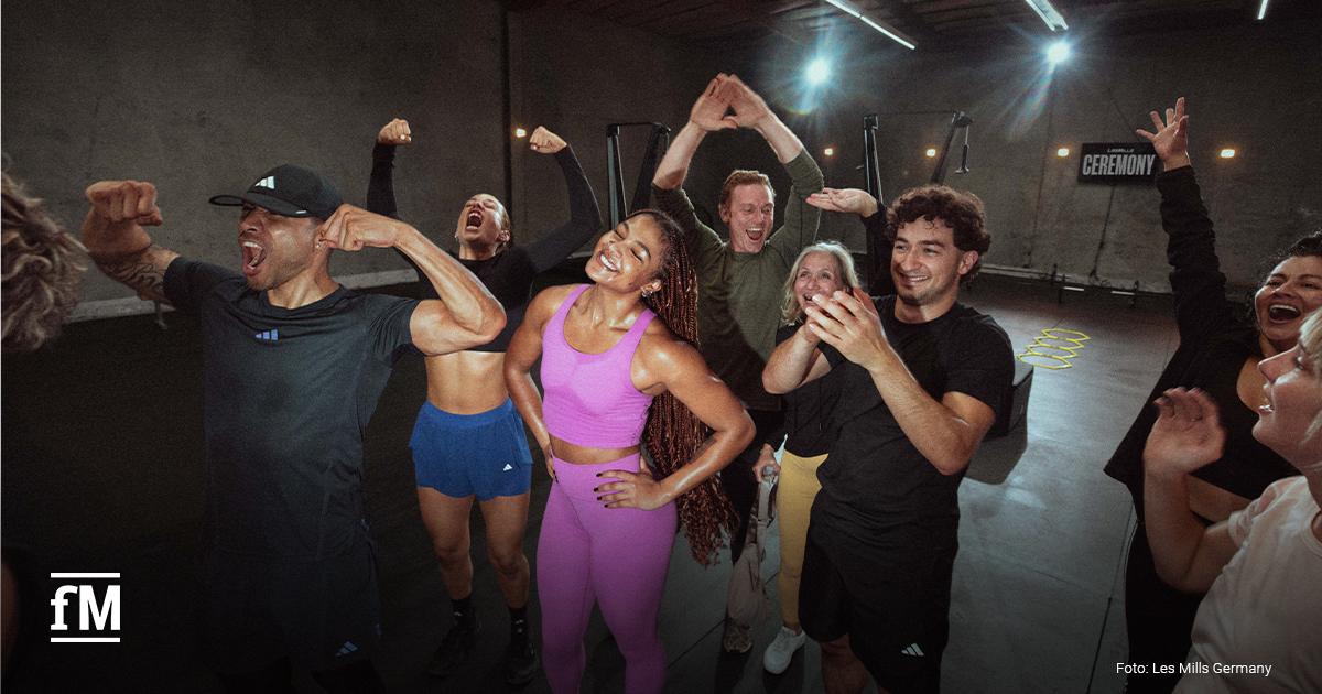 Eine Gruppe von Teilnehmenden jubelt gemeinsam nach einem absolvierten Workout in einem Kursraum.