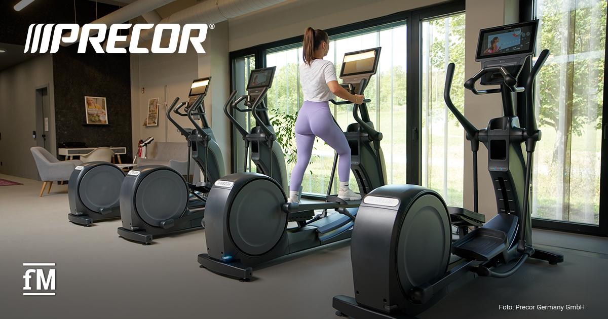 Eine Frau trainiert allein auf einem Crosstrainer vor großen Fenstern in einem hellen, modernen Fitnessbereich.