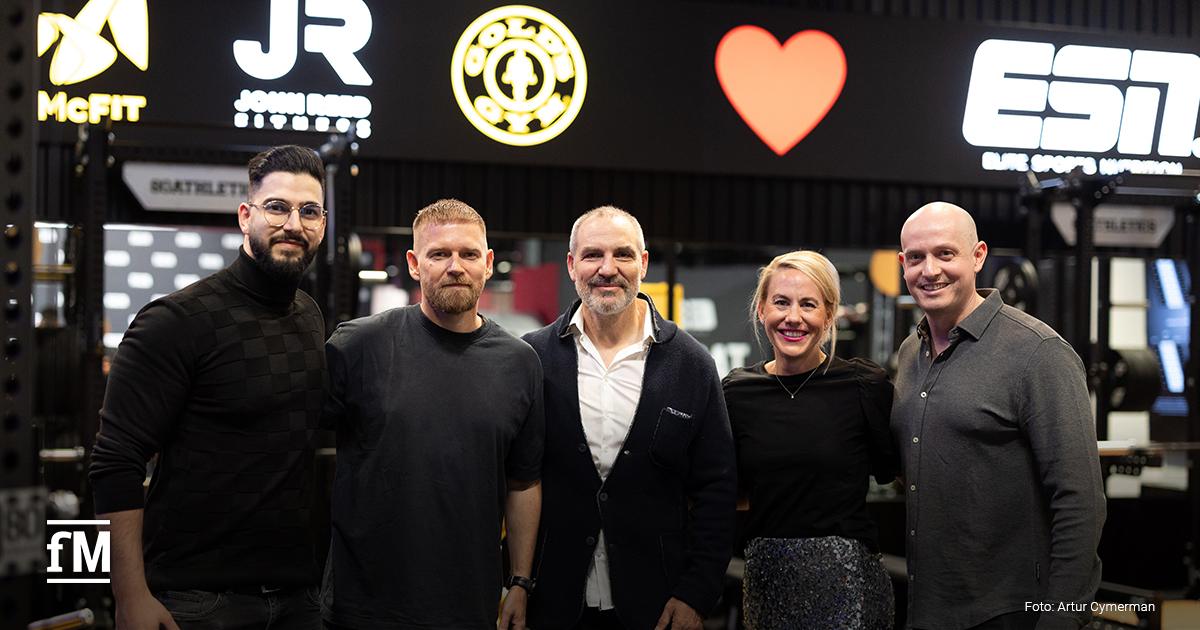 Fünf Personen (v. l. Ali Khadra, Philipp Markmann, Hagen Wingertszahn, Mary-Jo Slipek, Sascha Linz) stehen nebeneinander und lächeln in die Kamera. Sie befinden sich in einem Fitnessstudio. Im Hintergrund sind beleuchtete Logos der Marken McFIT, John Reed, Gold’s Gym, ein rotes Herzsymbol und das Logo von ESN in weißer Schrift auf schwarzem Grund zu sehen.