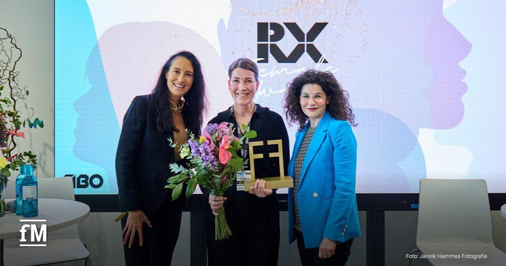 Gewinnerin Anna Martin-Niedecken (Mitte) wurde auf der FIBO-Bühne von Schirmherrin Tina Müller ausgezeichnet. In ihren Händen hält sie den RX Female Award und einen bunten Blumenstrauß.
