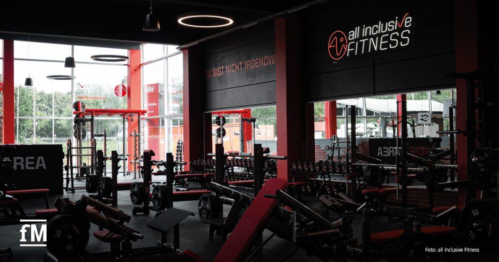 Innenansicht eines modernen Fitnessstudios mit Trainingsgeräten und dem Logo von all inclusive Fitness im Hintergrund.