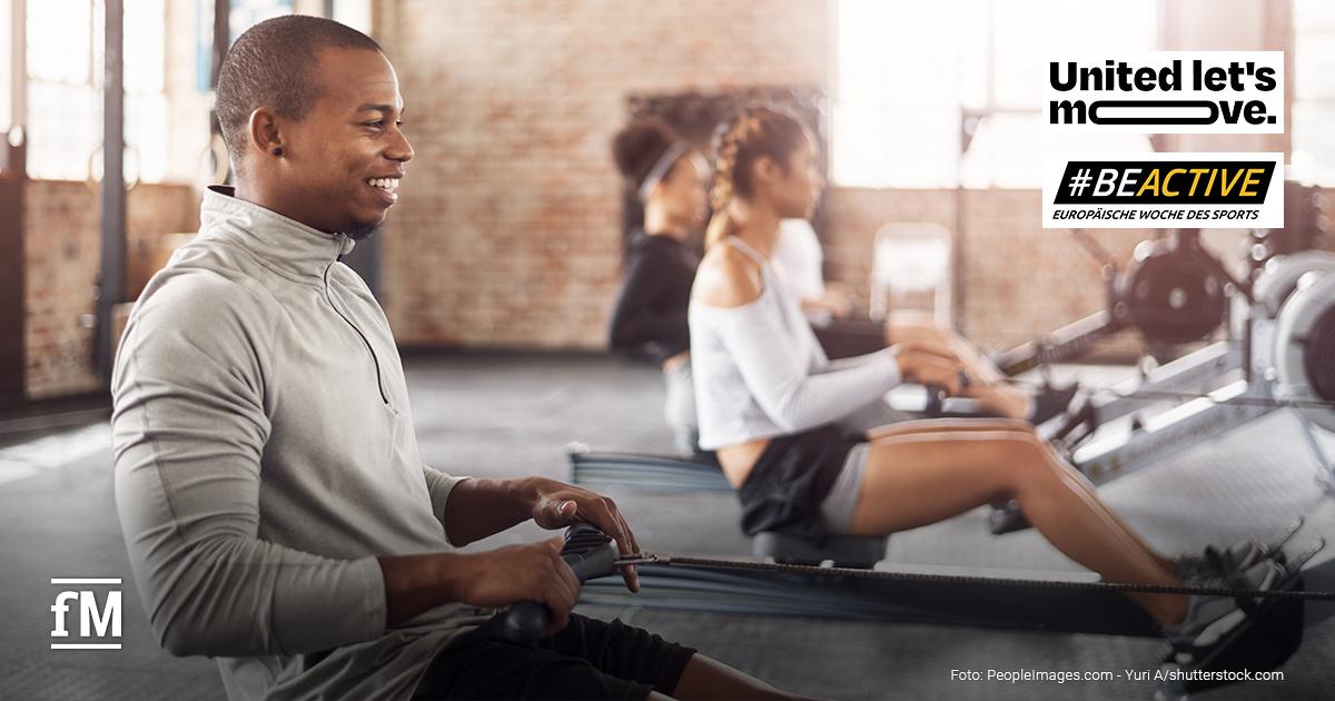 Mehrere Personen trainieren gemeinsam an Ruderergometern in einem lichtdurchfluteten Fitnessstudio mit Backsteinwänden. Im Fokus steht ein junger Mann in hellem Sportoberteil, der motiviert und lächelnd trainiert. Rechts oben ist das Logo der Kampagne '#BEACTIVE – Europäische Woche des Sports' und 'United lte's move!' zu sehen.