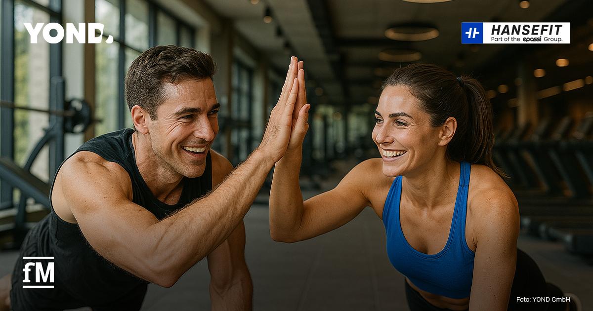 Ein Mann und eine Frau machen gemeinsam Sport in einem Fitnessstudio. Beide stützen sich auf den Unterarmen ab und lächeln sich an, während sie sich mit der freien Hand ein High-Five geben. Im Hintergrund sind Trainingsgeräte, eine große Fensterfront und die Logos von YOND und Hansefit zu sehen.