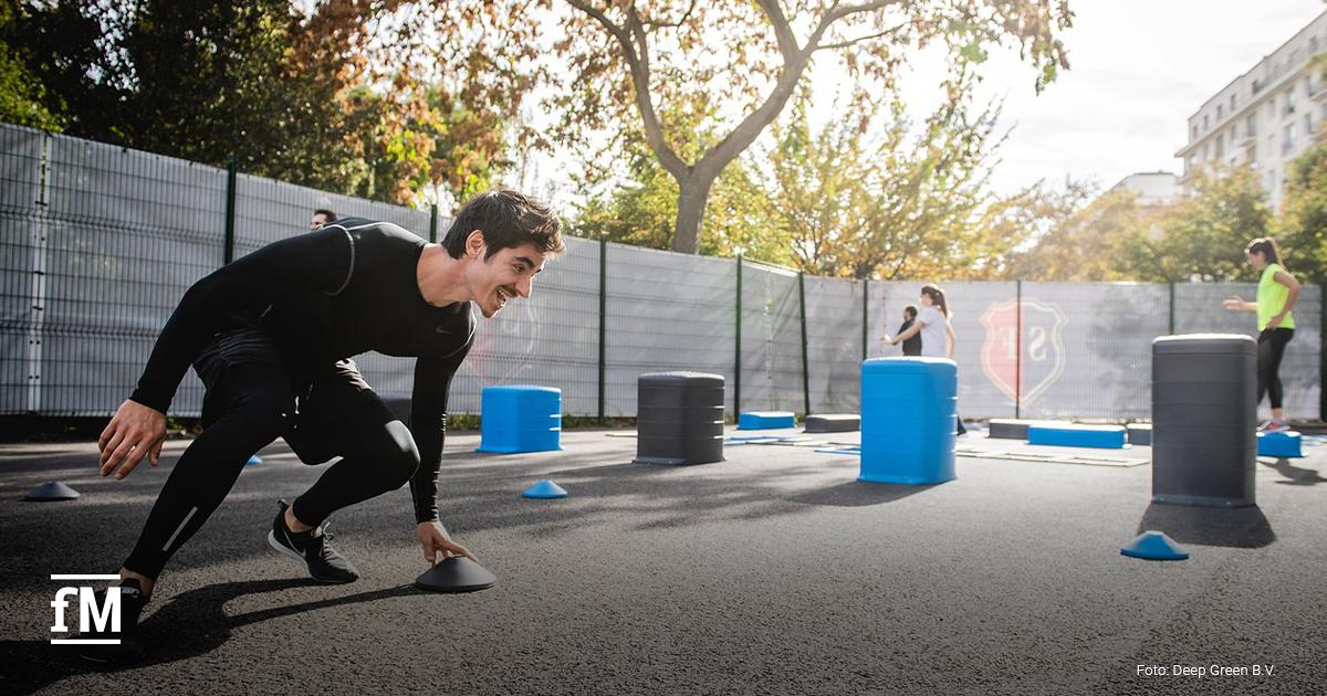 Ein sportlich aktiver Mann beim funktionellen Outdoor-Training, der mit Energie einen Parcours absolviert. Im Hintergrund trainieren weitere Personen.