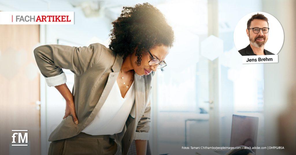 Eine Frau im Business-Outfit steht in einem hellen Büro und greift sich mit schmerzverzerrtem Gesicht an den unteren Rücken – ein Hinweis auf Rückenschmerzen durch schlechte Ergonomie oder Bewegungsmangel. Links oben steht „FACHARTIKEL“, rechts oben ist ein Porträtfoto von Jens Brehm eingeblendet, dem Autor des Artikels. Unten links ist das Logo von fitness MANAGEMENT (fM) zu sehen.
