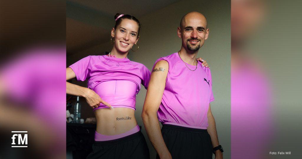 Zwei Sportler (Esther und Hendrik Pfeiffer) in pinker Laufkleidung stehen nebeneinander. Die Frau zeigt auf ihren unteren Bauch, wo ein feels.like-Schriftzug zu sehen ist. Auch der Mann hat das Branding auf dem Oberarm.