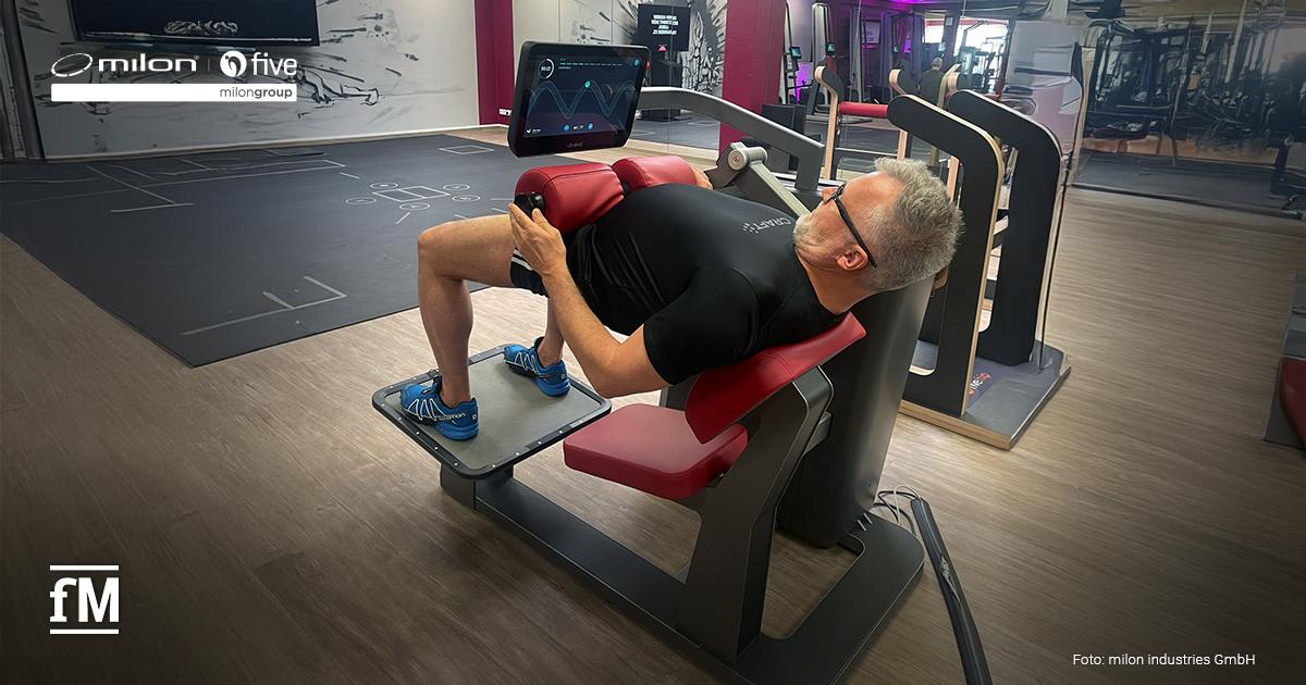 Ein Trainingsgerät vom Typ milon Q+ Hip Thrust in einem Fitnessstudio mit einer trainierenden Person, frontal aufgenommen, gut sichtbar sind Rückenpolster und Display.