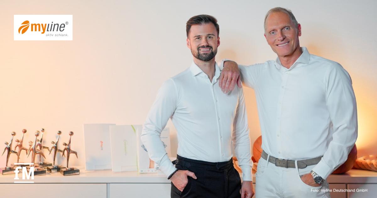 Eric Herrforth (links) und Alexander Dillmann stehen nebeneinander in einem hell ausgeleuchteten Raum mit weißer Wand. Beide tragen weiße, langärmelige Hemden. Dillmann lehnt mit dem rechten Arm auf der Schulter von Herrforth und lächelt in die Kamera. Vor ihnen steht ein Sideboard mit mehreren Trophäen und Ordnern. Links oben im Bild ist das orangefarbene Logo von myline zu sehen, rechts unten der Fotohinweis 'Foto: myline Deutschland GmbH'.