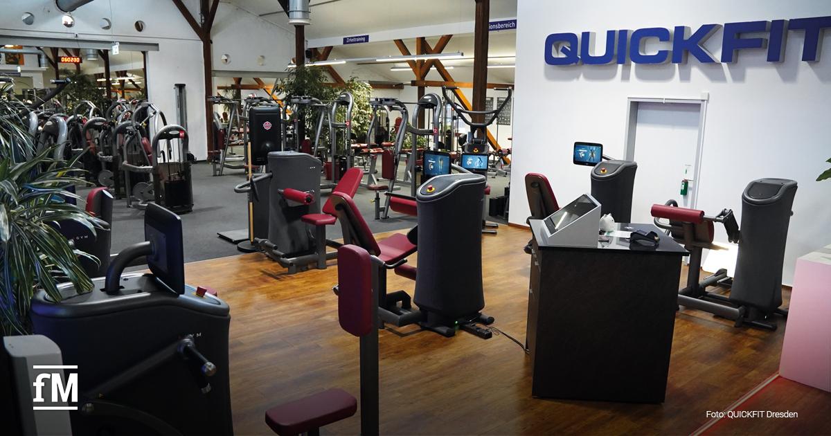 Trainingsfläche mit elektronischen Geräten, Touchscreens und einer zentralen Station. Rechts an der Wand prangt ein großes QUICKFIT-Logo. Viele Pflanzen lockern das Ambiente auf.