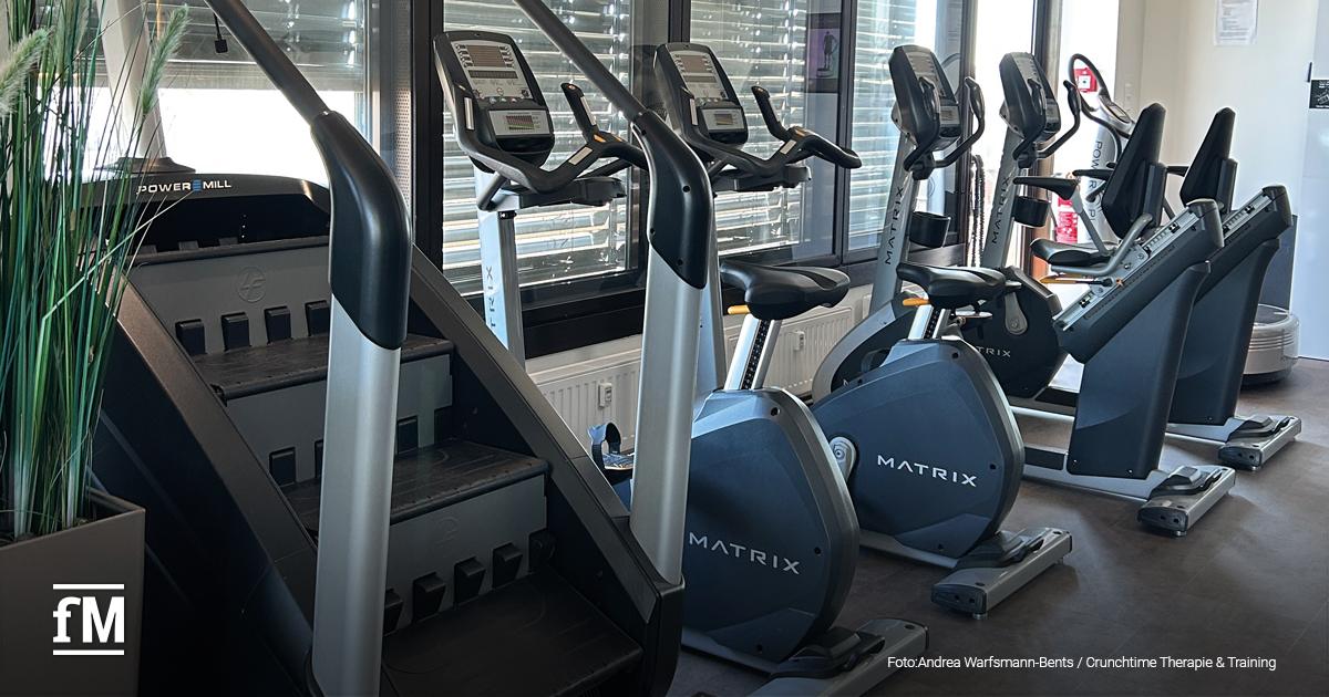 Heller Trainingsbereich im Crunchtime mit mehreren Cardiogeräten: zwei PowerMill-Treppensteiger, vier Fahrradergometer und drei Crosstrainer der Marke Matrix stehen vor großen Fenstern mit Jalousien. Links im Bild ein Dekopflanzengefäß.