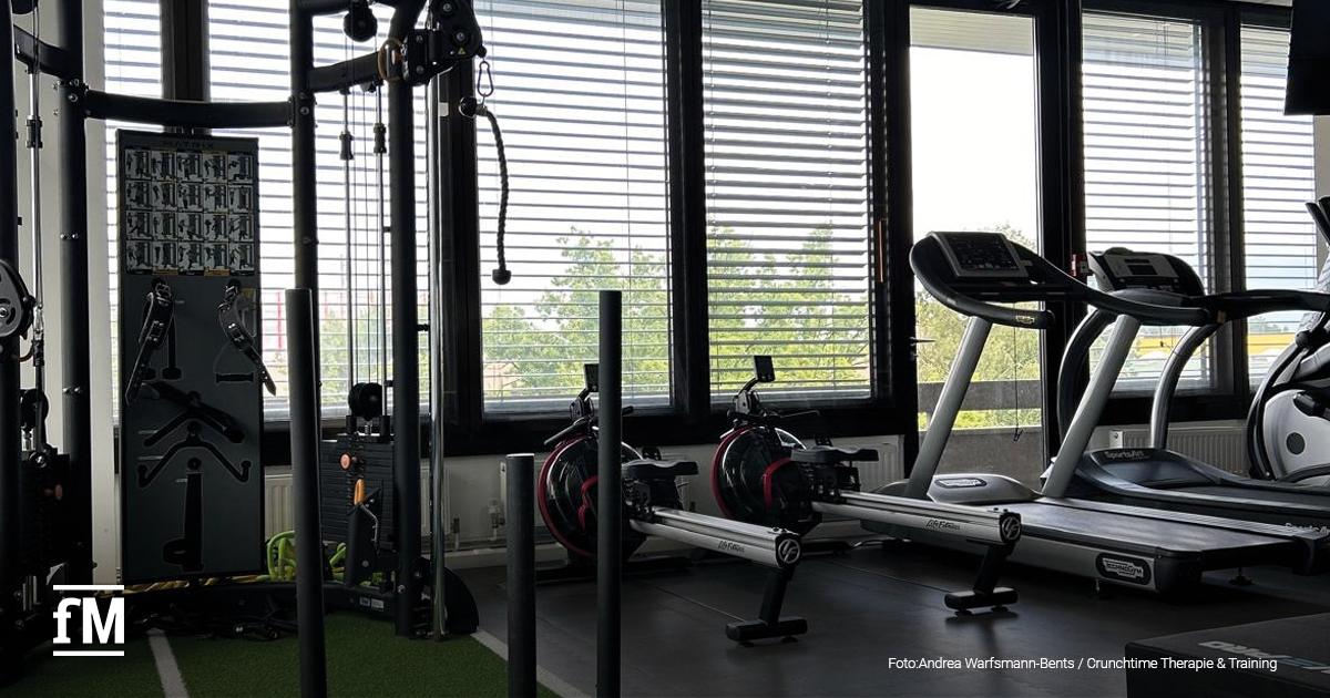 Trainingsbereich im Crunchtime mit mehreren Laufbändern, Rudergeräten und einem Kabelzugturm. Der Raum ist lichtdurchflutet, mit breiter Fensterfront und Sicht ins Grüne. Trainingszubehör wie Hanteln und Matten ist seitlich platziert.