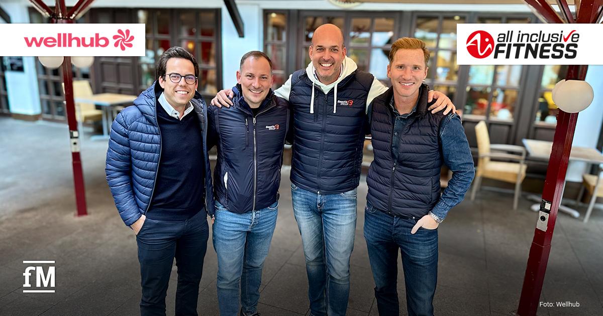 Vier lächelnde Vertreter von Wellhub und all inclusive Fitness stehen Arm in Arm unter einem Pavillon und tragen sportlich-legere Kleidung. Im Hintergrund sind die Logos der beiden Unternehmen zu sehen.
