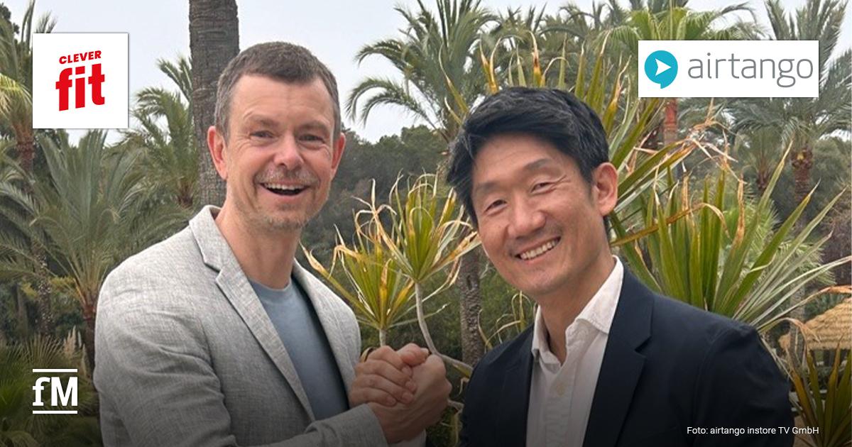 Riccardo Christ (links) und Chang-Hun Jo geben sich freundschaftlich die Hand. Christ trägt ein graues Sakko, Chang-Hun Jo ein schwarzes Sakko mit weißem Hemd. Oben links ist das Logo von clever fit, oben rechts das airtango-Logo.