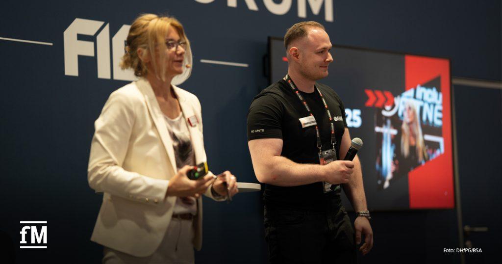 Zwei Vortragende stehen auf der Bühne des „FIBO Future Forum“. Links eine Frau im weißen Blazer, leicht unscharf, rechts ein Mann im schwarzen T-Shirt mit dem Slogan „NO LIMITS“. Beide halten Mikrofone, hinter ihnen läuft eine Präsentation mit rotem Design.