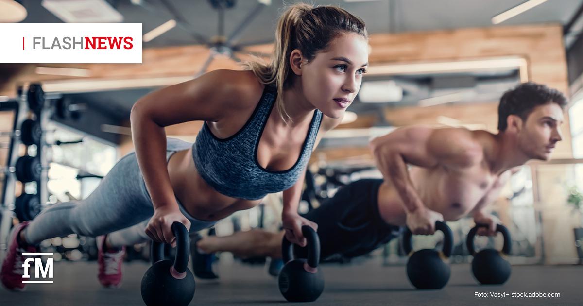 Eine Frau und ein Mann trainieren im Fitnessstudio mit Kettlebells in Liegestützposition.