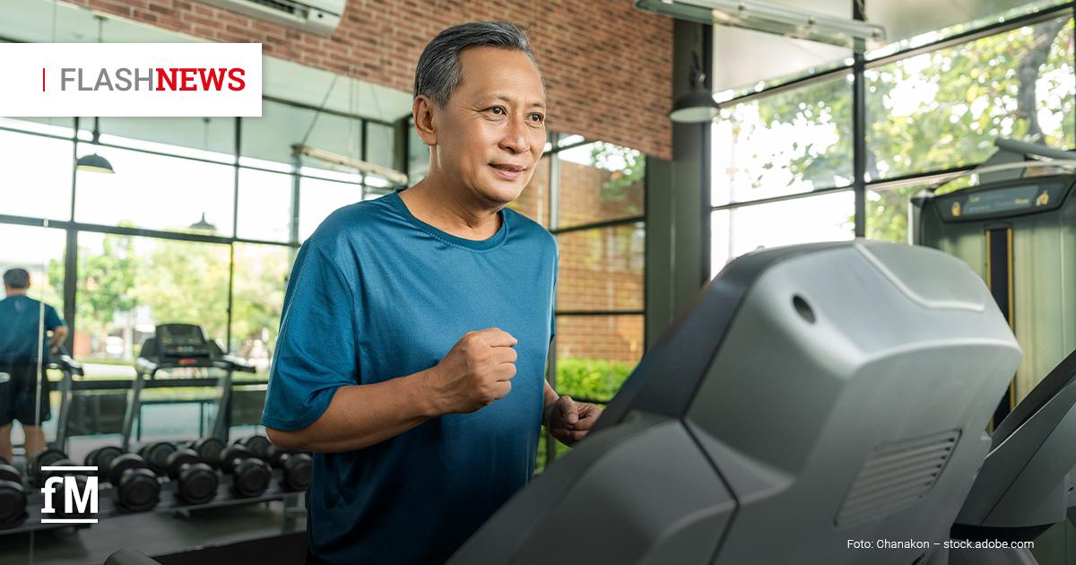 Ein älterer Mann mit grauen Haaren trägt ein blaues Sportshirt und joggt in einem hellen, modernen Fitnessstudio auf einem Laufband. Im Hintergrund stehen weitere Geräte und Hanteln, große Fenster lassen Tageslicht herein. Oben rechts steht der Hinweis 'Flashnews', die ersten fünf Buchstaben sind grau, die letzten vier rot.