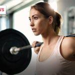 Junge Frau trainiert im Fitnessstudio mit einer Langhantel auf den Schultern, Fokus auf Konzentration und Anstrengung beim Krafttraining