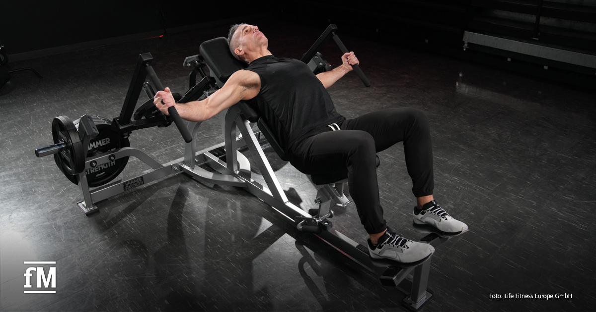 Ein älterer, sportlicher Mann führt auf einer schrägen Hammer Strength-Maschine eine Brustübung aus.