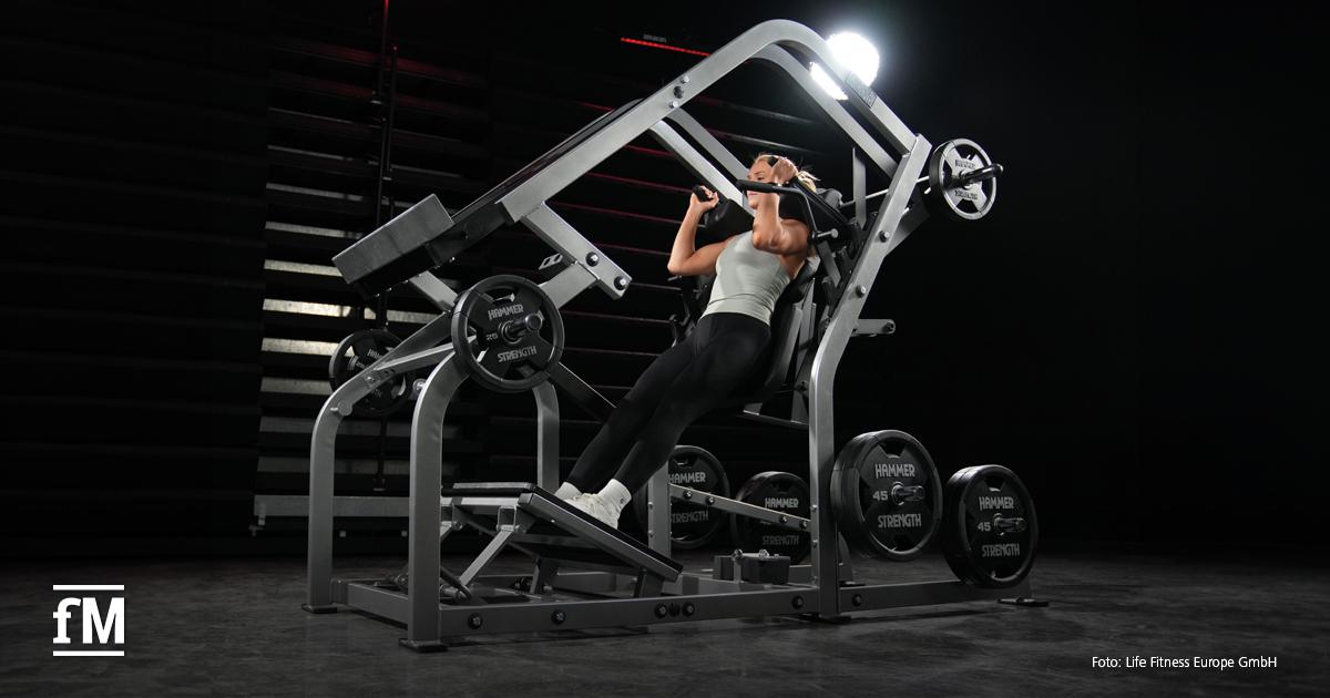 Eine Frau mit Sportkleidung trainiert auf einer vertikal geneigten Hammer Strength-Maschine.