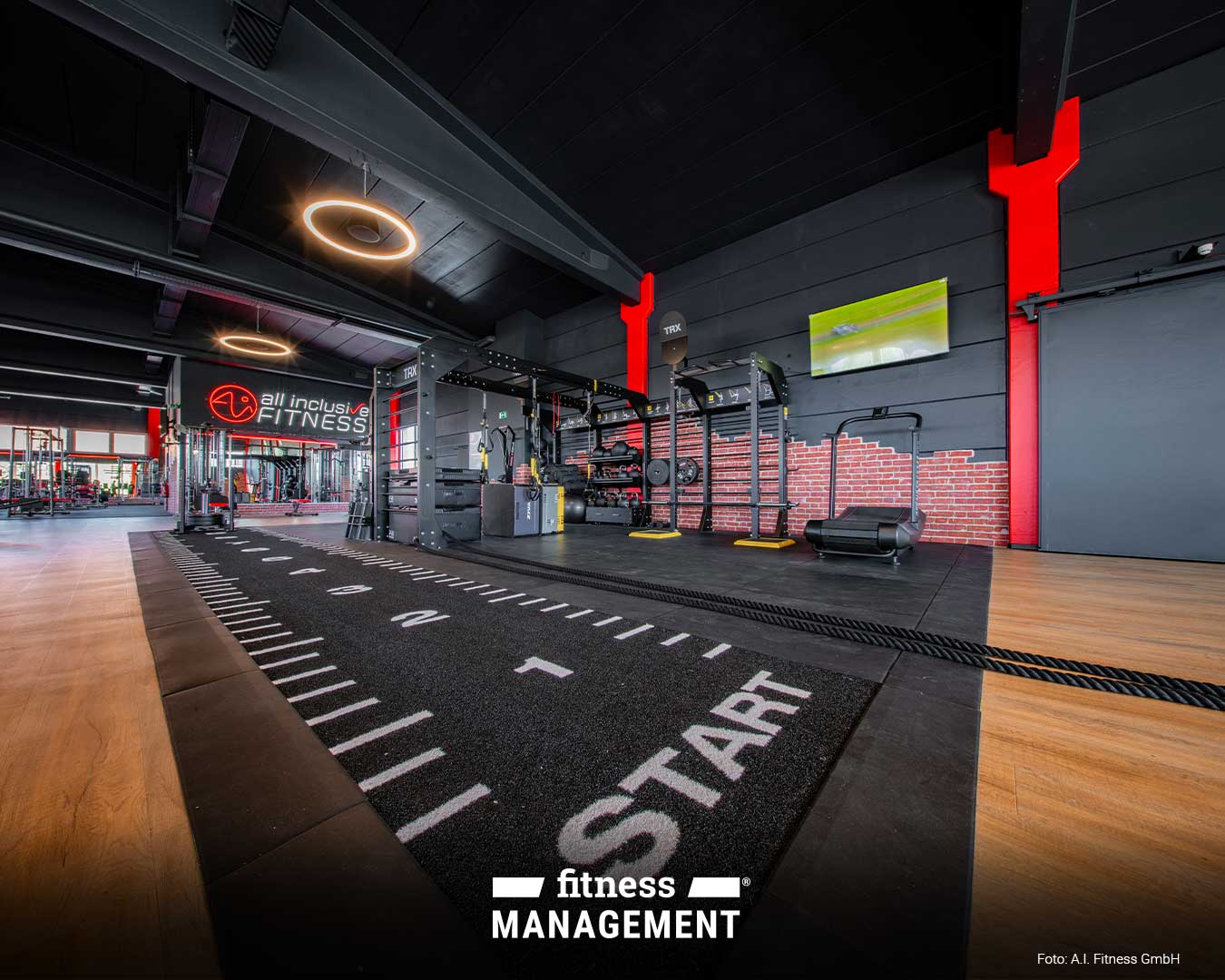 Moderner Functional-Training-Bereich mit Sprintstrecke und 'START'-Markierung im Vordergrund; rechts Trainingsgeräte und eine TV-Wand, links das beleuchtete Logo 'all inclusive FITNESS'.