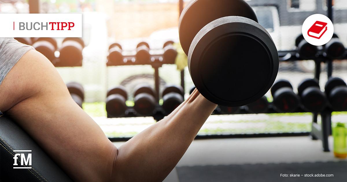 Eine Person in einem Fitnessstudio führt auf einer Trainingsbank eine Bizepsübung mit einer Kurzhantel aus. Im Hintergrund sind viele weitere Hanteln zu sehen.