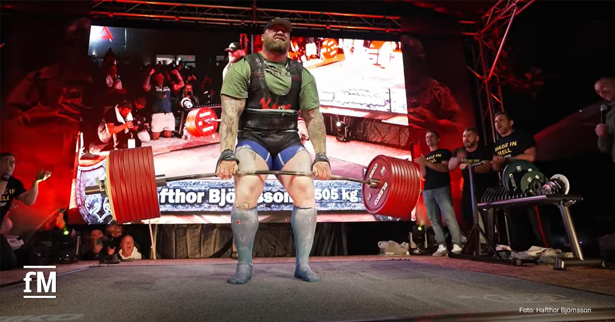 Ein Strongman-Athlet hebt bei einem Wettkampf eine mit vielen roten Gewichtsscheiben beladene Langhantel vom Boden; im Hintergrund jubeln Zuschauer, auf einer großen Leinwand ist der Name 'Hafthor Björnsson' und das Gewicht '505 kg' zu sehen.