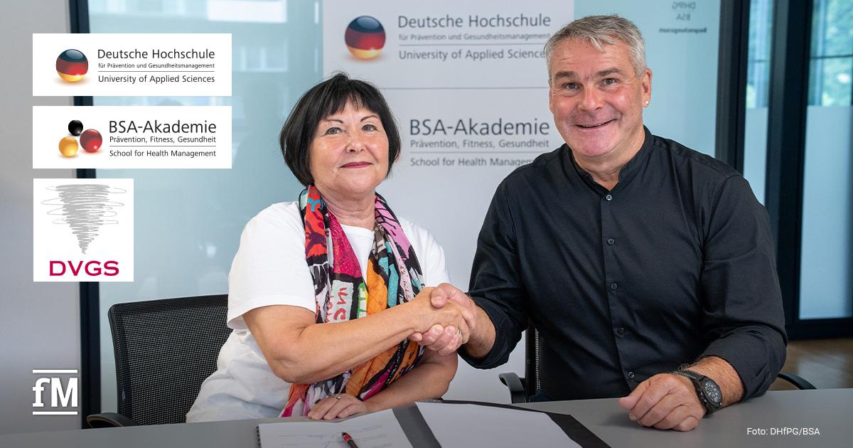 Zwei Personen sitzen an einem Tisch und reichen sich die rechte Hand zum Handschlag. Links sitzt eine Frau mit dunklem, kinnlangem Haar, weißem T-Shirt und buntem Schal. Rechts sitzt ein Mann mit grauem Haar in schwarzem Hemd. Auf dem Tisch liegt ein geöffneter Ordner mit Dokumenten und einem roten Stift. Im Hintergrund steht ein Schild mit den Logos und Namen der Deutschen Hochschule für Prävention und Gesundheitsmanagement und der BSA-Akademie.