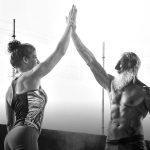 Ein Schwarzweißfoto zeigt: eine Frau und einen älteren, muskulösen Mann mit langem Bart. Beim Training geben sie sich ein High-Five.