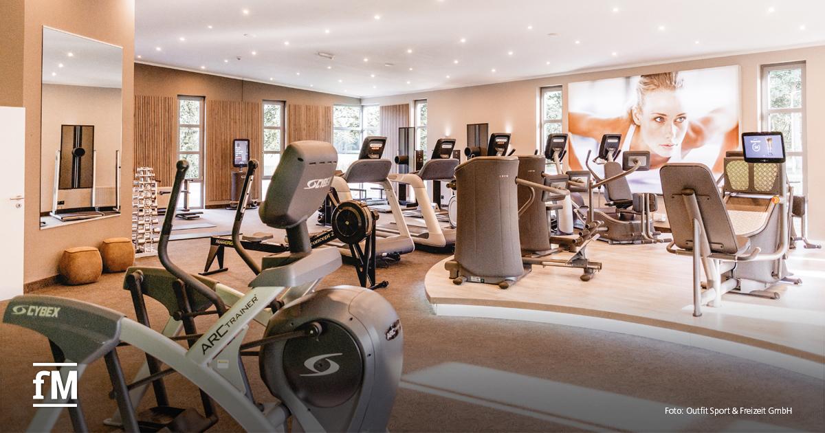 Fitnessraum mit modernen Cardiogeräten, hell beleuchtetem Ambiente und großem Wandbild einer trainierenden Frau.