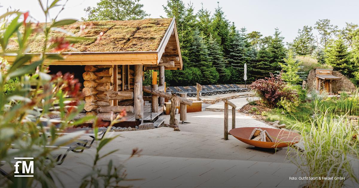 Außenbereich mit rustikaler Sauna aus Naturholz, Liegestühlen und üppiger Bepflanzung.