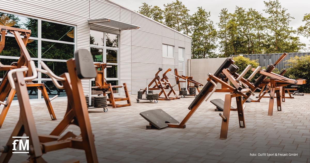 Outdoor-Trainingsbereich mit robusten Fitnessgeräten und Hantelscheiben auf einem gepflasterten Platz.