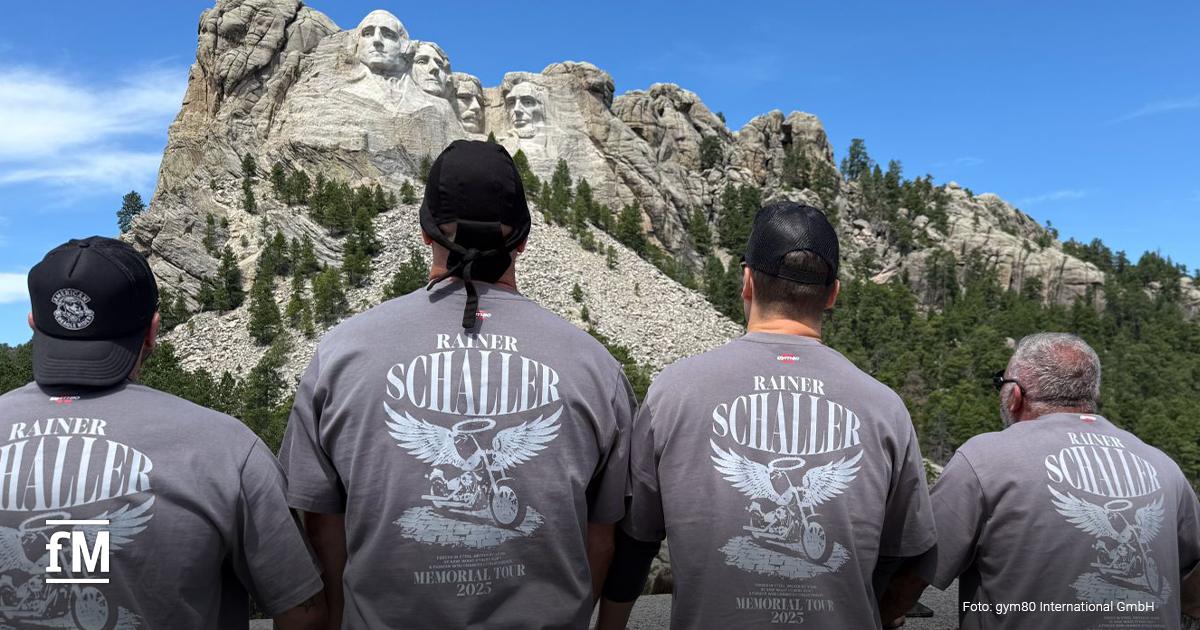 Vier Männer mit grauen T-Shirts der 'Rainer Schaller Memorial Tour 2025' stehen mit dem Rücken zur Kamera und blicken auf das Mount Rushmore Nationaldenkmal mit den in Stein gehauenen Gesichtern von vier US-Präsidenten.