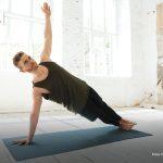 Ein Mann stützt sich seitlich auf einer Matte ab und hebt einen Arm in einem Raum mit großen Fenstern, der hell erleuchtet ist. Oben rechts ist ein rundes Portraitbild der Autorin Manuela Reusing abgebildet.