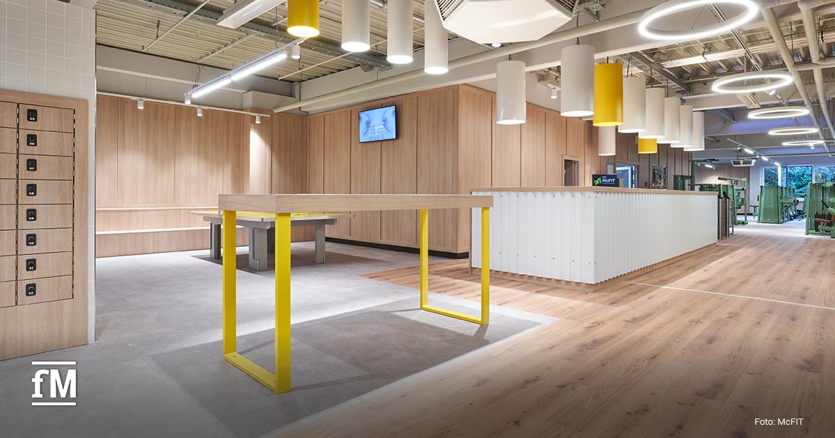 Moderner Eingangsbereich mit Holzboden, gelben Akzenten und modernen Lampen im neuen McFIT Original-Design.