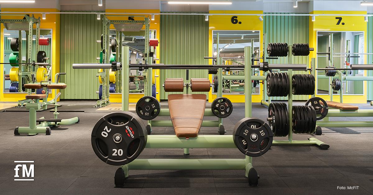 gym80 Hantelbank mit Langhantel, Hantelscheiben und Racks in einem McFit-Fitnessstudio.