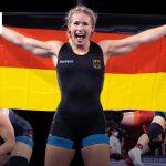 Eine erfolgreiche deutsche Ringerin jubelt mit der Deutschlandfahne in den Händen. Im Hintergrund laufen weitere Szenen aus Ringkämpfen.