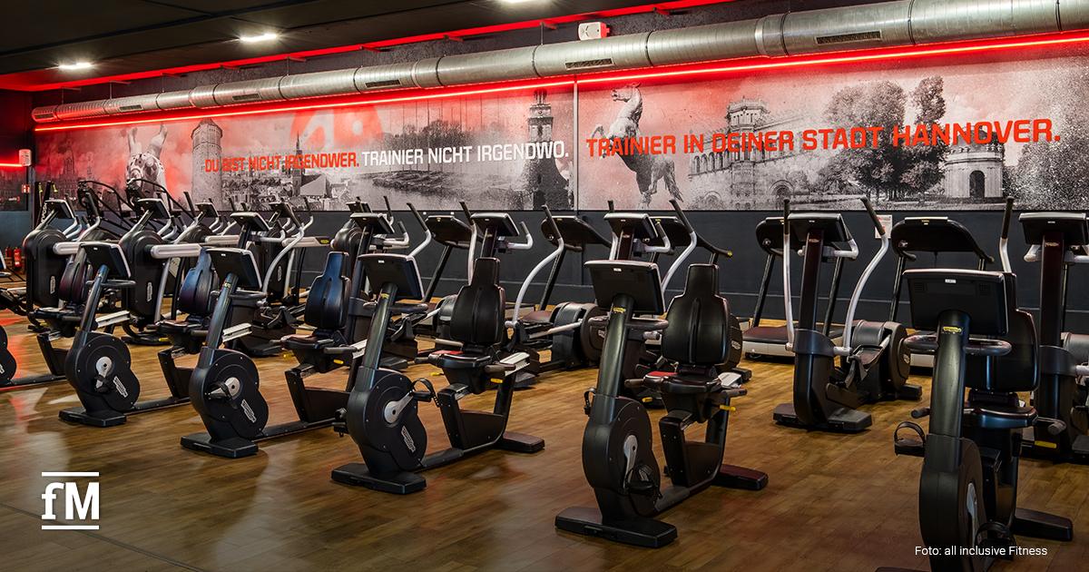 Reihe von Fitnessgeräten in einem Cardio-Bereich mit einer Wandaufschrift „Trainier in deiner Stadt Hannover“.