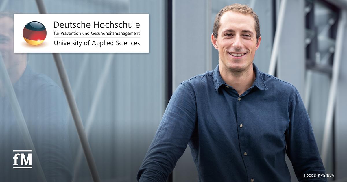 Ein Mann (Andreas Barz) im blauen Hemd steht lächelnd vor einem modernen Gebäude, links oben das Logo der Deutschen Hochschule für Prävention und Gesundheitsmanagement (DHfPG).