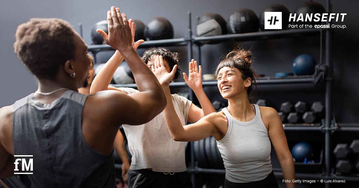 Gruppe von drei Personen im Fitnessstudio klatscht sich lachend beim Training ab.
