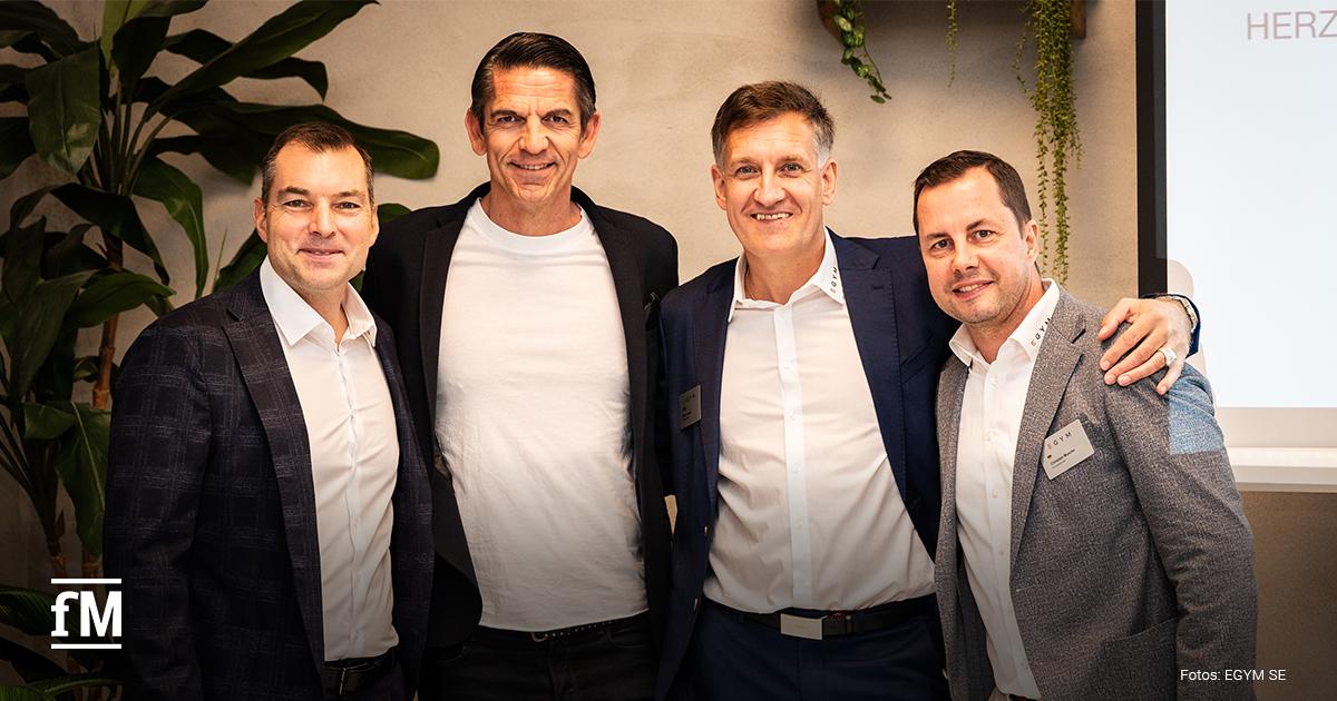 Vier Männer in Businesskleidung stehen nebeneinander und posieren für ein Gruppenfoto